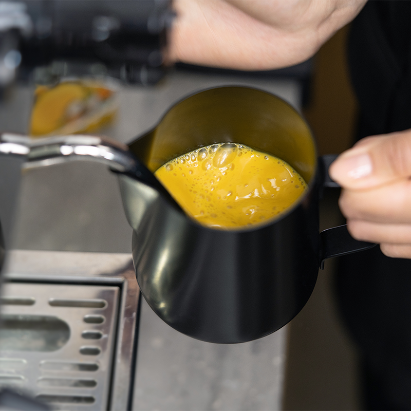 Kubek z żółtym napojem spieniany w maszynie do spieniania mleka